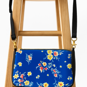Crossbody Purse, fabric body with a smooth surface and a vivid blue background. Bright floral print in yellow, white, and reddish-orange tones, giving it a cheerful, summery feel.  Gold-tone zipper and swivel clasps attach the strap. Adjustable black straps can be worn crossbody or over the shoulder.